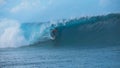 Extreme male rider surfing in breathtaking Tahiti catches a big emerald wave.