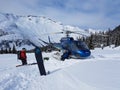 Extreme snowboarder and pilot talk by the blue helicopter parked in mountains.