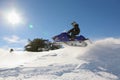 Snowmobile rider jumping machine on sunny hillside