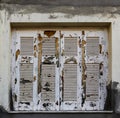 Extremely chipped and weather-worn white paint on closed grungy wooden shutters in stucco building with grey paint smeared abound