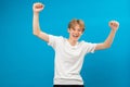 Extremely excited teen boy shouting making yes gesture, amazed with his victory, triumph. Indoor studio shot isolated on blue