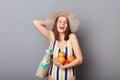 Extremely happy caucasian woman wearing striped swimsuit and straw hat  gray background holding oranges in hands rejoicing Royalty Free Stock Photo