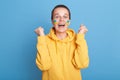 Extremely happy Caucasian woman in yellow hoodie with Ukrainian flag on cheeks, hearing news about Ukraine victory, stop war, Royalty Free Stock Photo