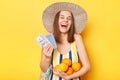 Extremely happy cheerful woman wearing striped swimsuit and straw hat isolated yellow background holding oranges passport and Royalty Free Stock Photo