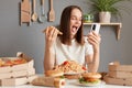 Extremely happy overjoyed Caucasian woman with brown hair wearing white t shirt sitting in kitchen at table and holding slice of Royalty Free Stock Photo