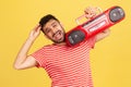 Extremely happy satisfied man with beard in striped red t-shirt holding red tape recorder on shoulders, enjoying listening to Royalty Free Stock Photo