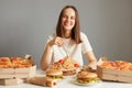 Extremely happy smiling beautiful woman with brown hair wearing white T-shirt sitting at table among fast food isolated over gray Royalty Free Stock Photo