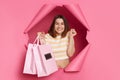 Extremely happy smiling brunette woman wearing striped t shirt posing in torn pink paper wall holding shopping bags clenched fist Royalty Free Stock Photo