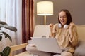 Extremely happy woman in knitted sweater using laptop sitting on couch at home doing online shopping betting winning lottery Royalty Free Stock Photo