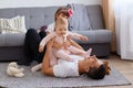 Extremely happy young adult man lying on floor near sofa and playing with his little kids, wearing white t shirt and trousers, Royalty Free Stock Photo