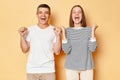 Extremely happy young couple friends man woman in casual clothing isolated over beige background clenched fists yelling happily Royalty Free Stock Photo