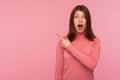 Extremely shocked brunette woman in pink sweater pointing away looking at camera with big eyes and open mouth, surprised with Royalty Free Stock Photo