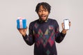 Extremely surprised pleased african guy with dreadlocks holding mobile phone with empty blank and gift box, online presents order