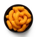 Extruded cheese puffs in a black ceramic bowl isolated on white. Top view