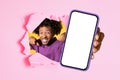 Exuberant man with curly hair joyfully pointing through a ripped pink paper, holding a smartphone Royalty Free Stock Photo