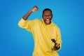 An exultant Black man in a yellow hoodie clenches his fist in a gesture of victory