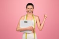 Exultant young woman celebrating her weight loss success, holding a scale and wearing a measuring tape