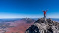 An exultant hiker stands with arms raised atop a rugged volcanic summit