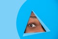 Eye of african-american man peeking throught triangle in blue background Royalty Free Stock Photo