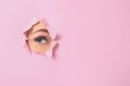 Eye of beautiful young woman visible through hole in pink teared paper Royalty Free Stock Photo