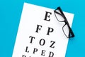 Eye examination. Eyesight test chart and glasses on blue background top view Royalty Free Stock Photo