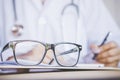 Eye glasses on desk with blur background of doctor writing prescription Royalty Free Stock Photo