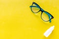 Eye health. Glasses with transparent optical lenses and eye drops on yellow background top view space for text closeup