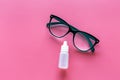 Eye health. Glasses with transparent optical lenses and eye drops on pink background top view copy space closeup