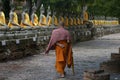 Eye-level shot of a monk walking around Buddha statues in Wat Yai Chaimongkol temple in Thailand Royalty Free Stock Photo