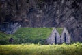 Eye-level shot of two stone houses with grass roofs in a field under a cliff in Iceland