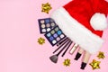 Makeup products in red Santa hat with golden gift bows on pink background. Christmas makeup concept with copy space Royalty Free Stock Photo