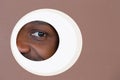 Eye of smiling african-american man peeking throught circle in brown background Royalty Free Stock Photo