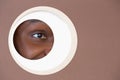 Eye of smiling african-american man peeking throught circle in brown background Royalty Free Stock Photo