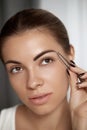 Eyebrow correction. Plucking eyebrows. Beautiful young woman with tweezers. Royalty Free Stock Photo