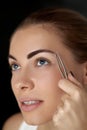 Eyebrow correction. Plucking eyebrows. Beautiful young woman with tweezers. Royalty Free Stock Photo