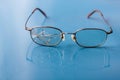 Eyeglasses with cracked lens on shiny blue background Royalty Free Stock Photo