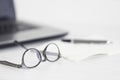 Eyeglasses, open notebook, pen and laptop on the office table.