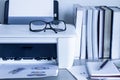 Eyeglasses on printer with books on wooden table