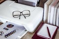 Eyeglasses on printer with books on wooden table