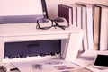 Eyeglasses on printer with books on wooden table