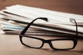 Eyeglasses and stack of newspapers on wooden desk for themes of ophthalmology, poor vision and reading Royalty Free Stock Photo