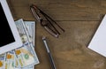 Eyeglasses on tablet pc with dollar bills and pen on wooden table at close up