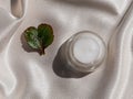 Eyelid cream glass jar with green heartshaped leaf on smooth white silk background shadow water splashes sunlight