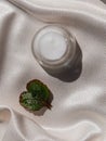 Eyelid cream glass jar with green heartshaped leaf on smooth white silk background shadow water splashes sunlight Royalty Free Stock Photo