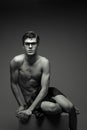 Eyewear concept. Beautiful handsome muscular male model with nice abs posing in trendy glasses undressed. Boy sitting on wooden