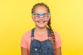 Eyewear fashion. Portrait of funny little girl in denim overalls wearing two stylish eyeglasses and smiling joyfully