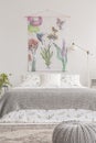 Fabric with flowers hanging on white wall in bright bedroom interior with metal lamp, double bed with floral sheets