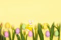 Fabric rabbit, souvenir eggs and flowers on a yellow background, copy space. Background for greeting holiday card for