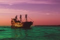 A fabulous golden vintage ship sailing on a surreal green sea against a purple - red sky, concept of fairy tales and magic