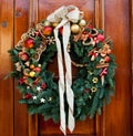 Fabulous outdoor Christmas wreath ornamented with artificial fruit against wooden door Royalty Free Stock Photo